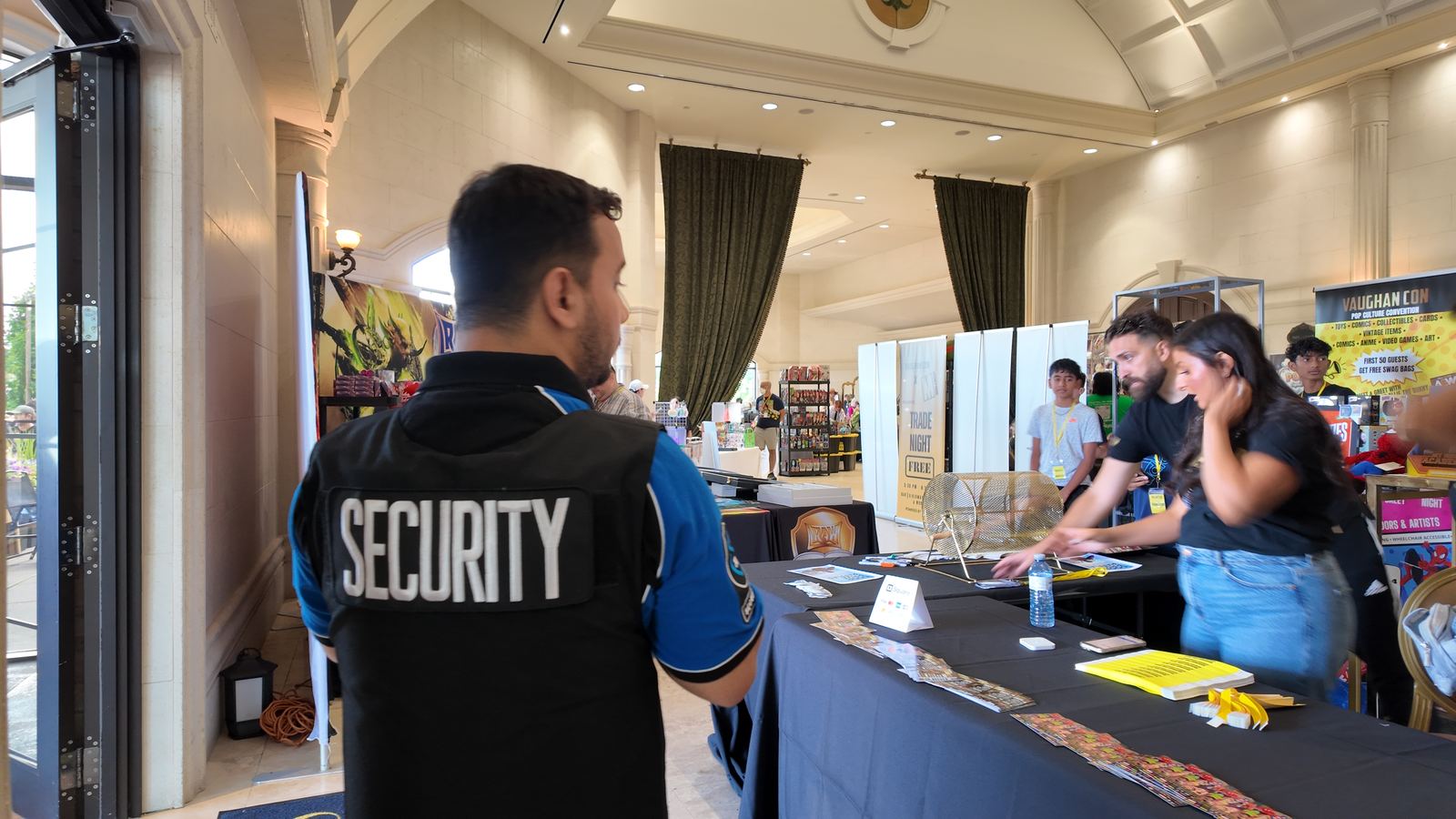 A KingsGuard guard standing beside a registration table inside an event hall while organisers set up
