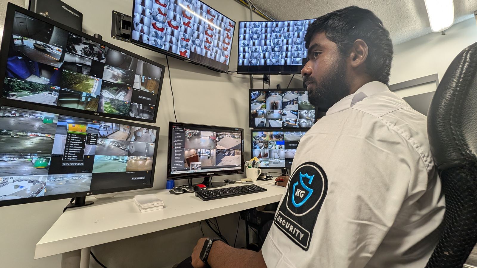 A KingsGuard operator in uniform watching a wall of monitors showing live camera views from several client properties