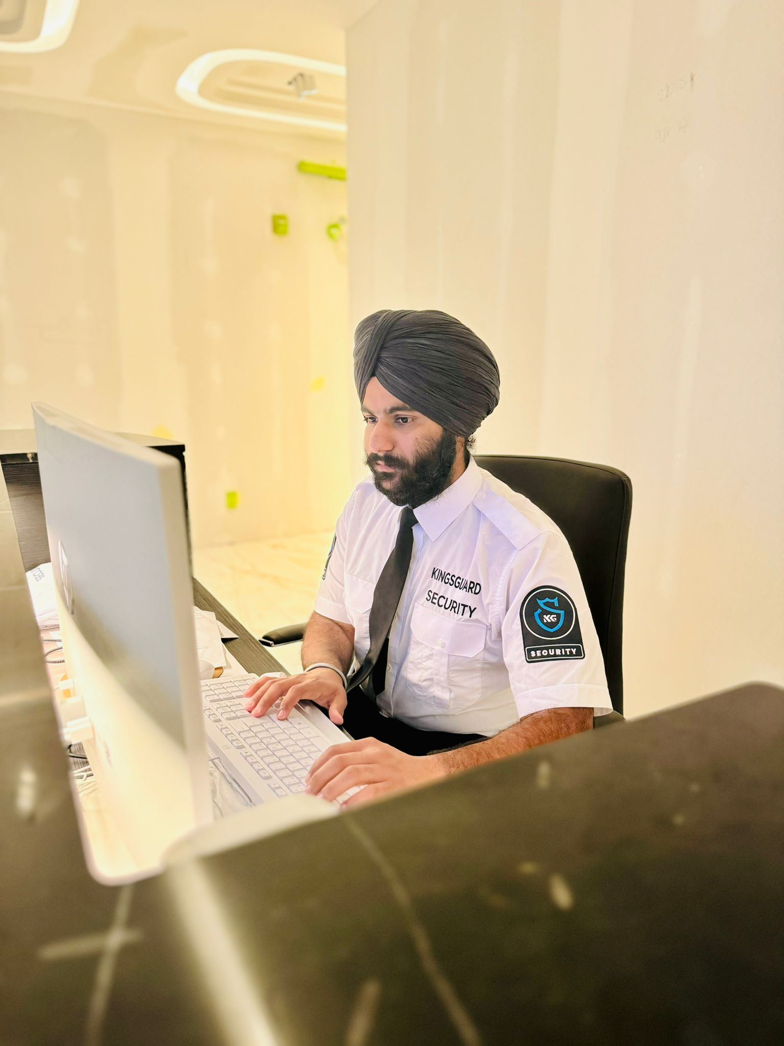 A KingsGuard concierge guard in a white uniform shirt and tie working at a residential lobby front desk computer